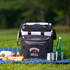 A black and white rolling cooler with a logo, placed on grass near picnic food and drinks.