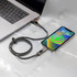 A grey charging cable connected to a laptop and a mobile phone, featuring a flexible design and a branding logo.