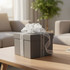 A grey gift box tied with a soft, white ribbon featuring a decorative bow, set on a wooden table.