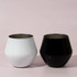 Two detachable wine glasses, one white and one black, displayed against a soft pink background.