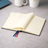 A black diary with cream pages opened to reveal weekly layouts, featuring coloured ribbon bookmarks.