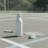 A drink bottle in white rests on a tennis court beside a racquet and shuttlecock. It features a logo.