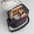 A cooler bag in black with a silver interior, containing a wooden board, snacks, and a bottle.