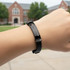 A black engraved bracelet is displayed on a wrist, featuring a decorative design and metallic accents.