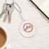 A clear PVC hand fan with a keychain, featuring a round shape, sits on a textured surface near a coffee cup and notebook.