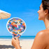 A colourful 20cm foldable fan featuring a vibrant design, held by a person at the beach.