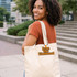 A woman with curly hair smiles while carrying a cream-coloured tote bag with a logo.