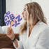 A heart-shaped wooden paper fan with a patterned design, held by a woman with wavy hair, wearing a white shirt.