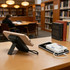 A wireless power bank with a charging cable, featuring a sleek design and a stand, placed on a library table.