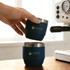 A stackable stainless steel tumbler in navy blue, featuring a logo, is being held above another tumbler on a table.