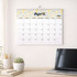 A wall calendar featuring a floral design and a section for April 2027, displayed with a plant and a laptop.