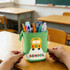 A green expandable pencil case featuring a school bus design, filled with pens, pencils, and scissors.