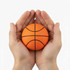 An orange basketball held in two hands, featuring black lines for seam details. The hands cradle the ball gently.