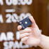 A black luggage lock with a keypad and a metal loop, held in a hand against a blurred background.