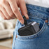 A compact grey magnetic wireless charging station being placed in a pocket of denim jeans.