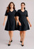 Two women wearing black extended short sleeve dresses, featuring a V-neck and a flared skirt. The dresses have a simple design.