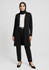 A black longline cardigan worn over a white top and black trousers, styled with a belt and a hijab.