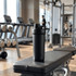 A drink bottle with a double-wall design in black, placed on a gym bench with exercise equipment in the background.