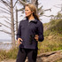 A woman stands outdoors holding binoculars, wearing a navy half-zip jacket amidst a natural landscape.