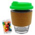 A glass coffee cup with a cork band and a bright green lid, accompanied by a pack of colourful jelly beans.