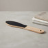 A wooden foot file with a light timber handle and a black abrasive surface, placed beside neatly folded cloths.