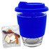 A blue reusable coffee cup with a silicone sleeve and a packet of jelly candy beside it. The cup has a logo.