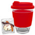 A reusable coffee cup with a red silicone sleeve and lid, accompanied by a pack of colourful jelly sweets.