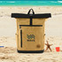 A khaki and black laptop backpack with a logo, placed on a sandy beach setting.