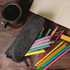 A grey felt utility case filled with colourful pens and markers, situated beside a coffee cup and an open notebook.