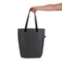 A hand holds a grey felt tote bag with black straps. The bag features a branding logo.