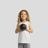 A child with curly hair wearing a white sleeveless tank top and grey shorts, holding a black basketball.