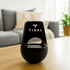 A black wireless speaker made from recycled ABS, featuring a logo, placed on a wooden table in a living room setting.
