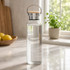 A drink bottle with a glass body, metal lid, and wooden top, featuring a sleek design and a logo.