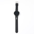 A black smart watch with a round face and a silicone strap, featuring a logo on the band.