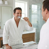 Colgate Wave Ultra-Compact Head Soft Toothbrush, Soft Bristles for Gentle Plaque Removal, Compact Curved Head for Hard-to-Reach Areas. View of a man brushing his teeth in a sunny bathroom