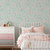 A girl's bedroom with a white metal bed with pink and white bedding, a dresser, and cherry blossom wallpaper with an aqua background.