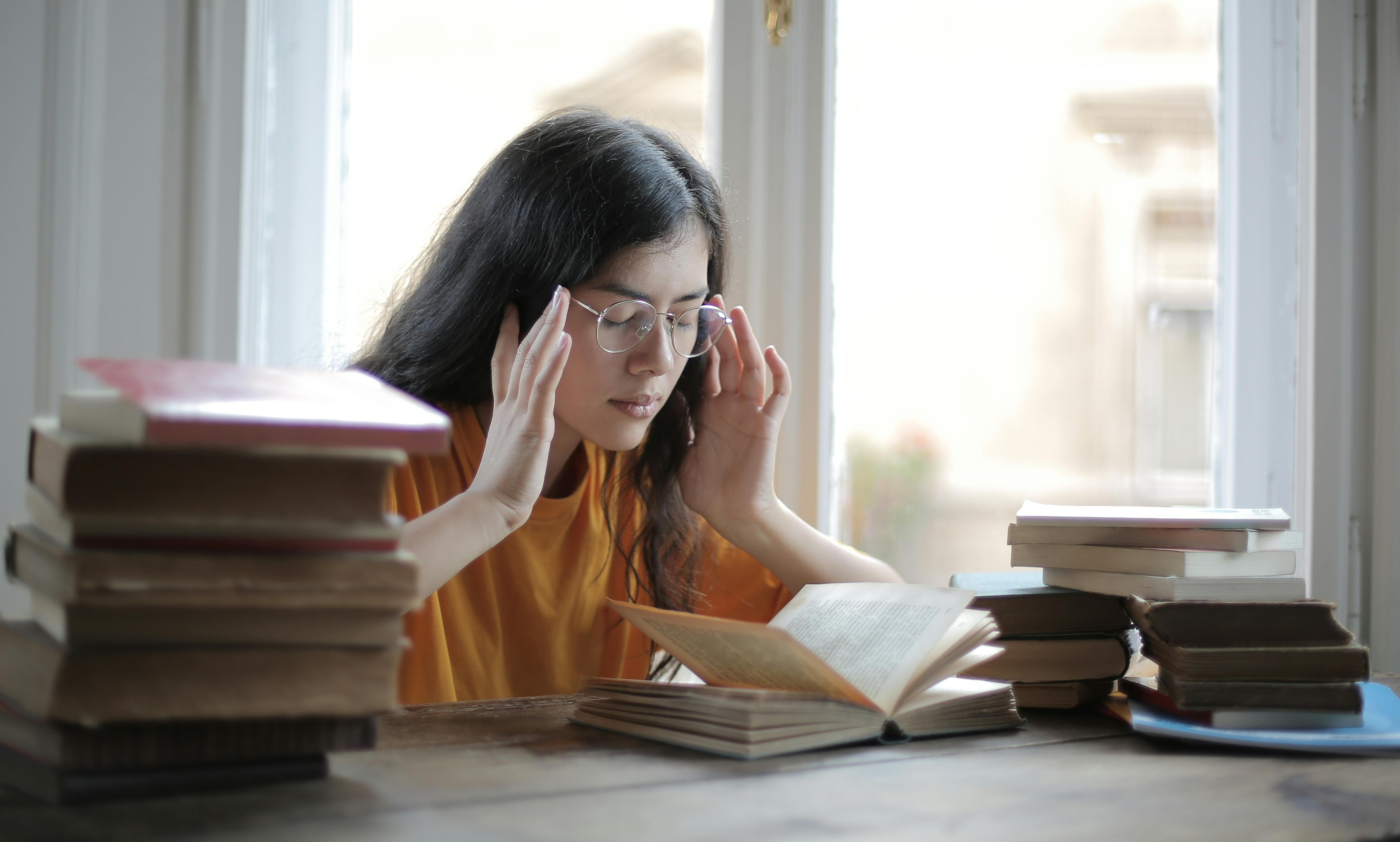 woman with a headache sitting at a desk reading a book
