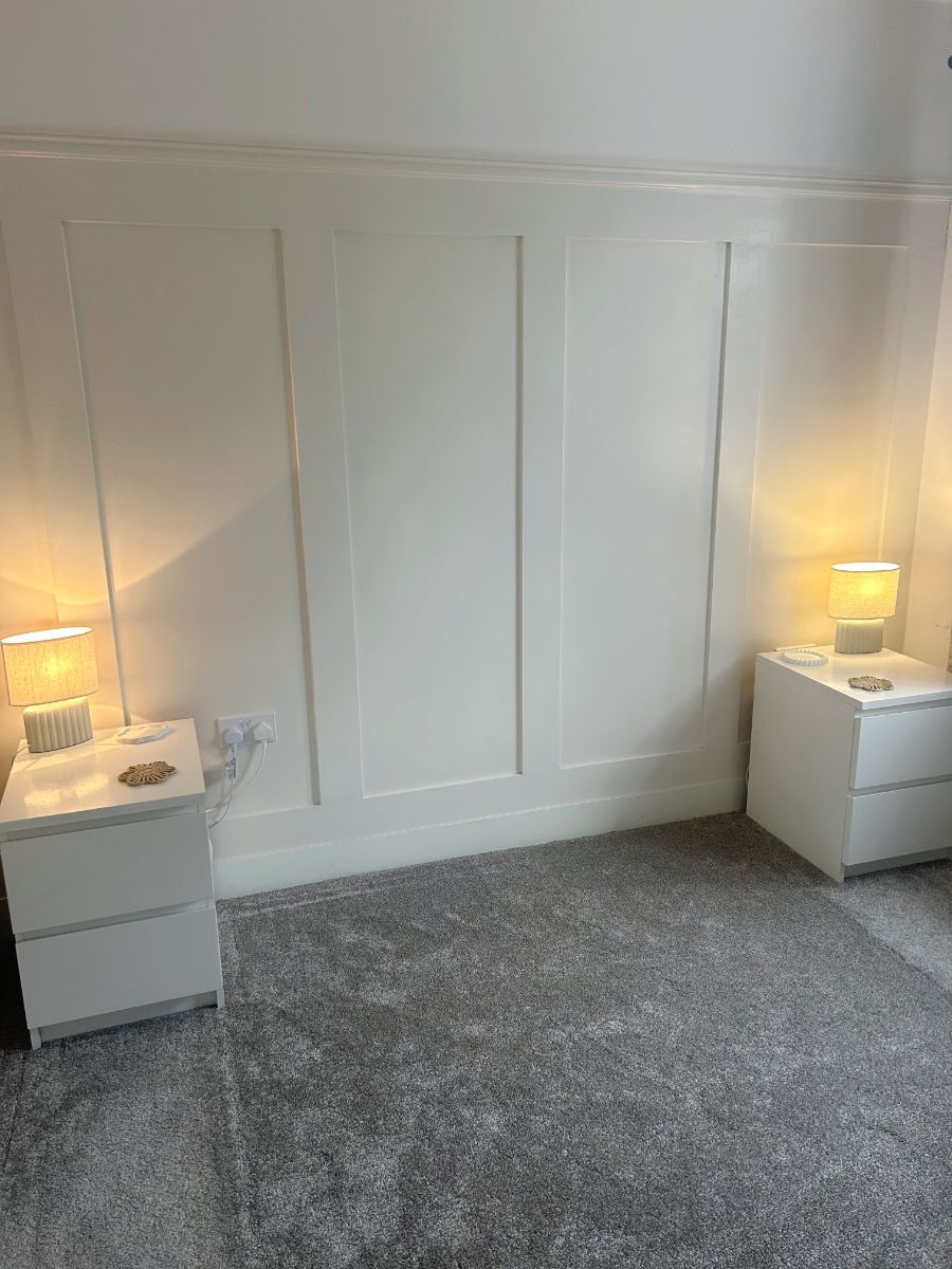 Bedroom with three-quarter height shaker wall panelling painted in a soft neutral shade, creating a warm and inviting atmosphere