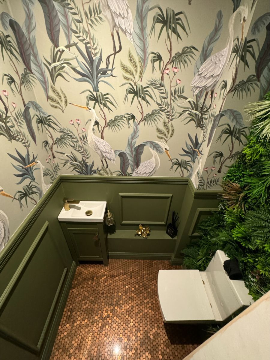 Eclectic bathroom with green half-wall wainscoting and decorative wallpaper above, featuring a flower wall panel behind the toilet