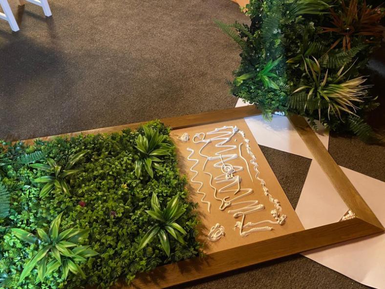 Applying adhesive to frame and positioning artificial plant tiles for green wall panel