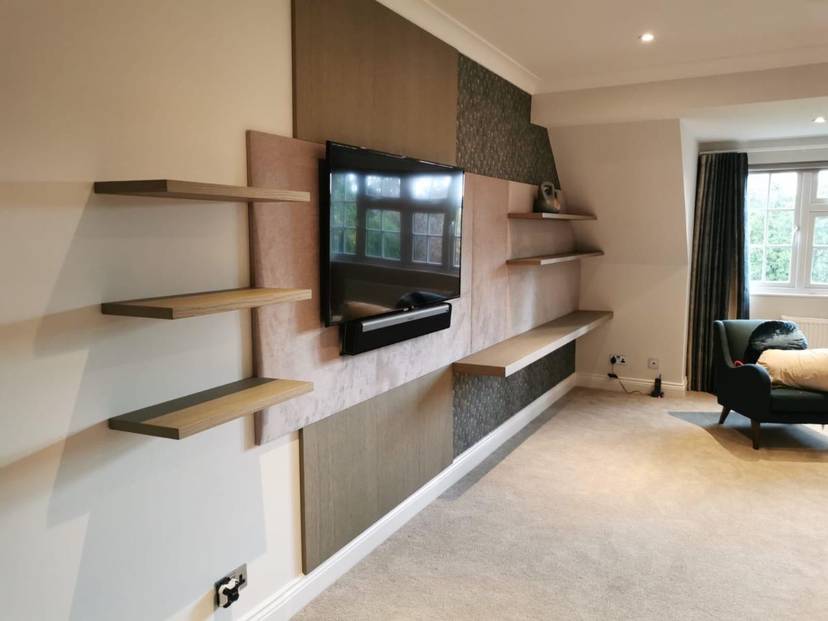 Elegant curated media wall with upholstered panel behind television, surrounded by wooden panels and integrated floating shelves
