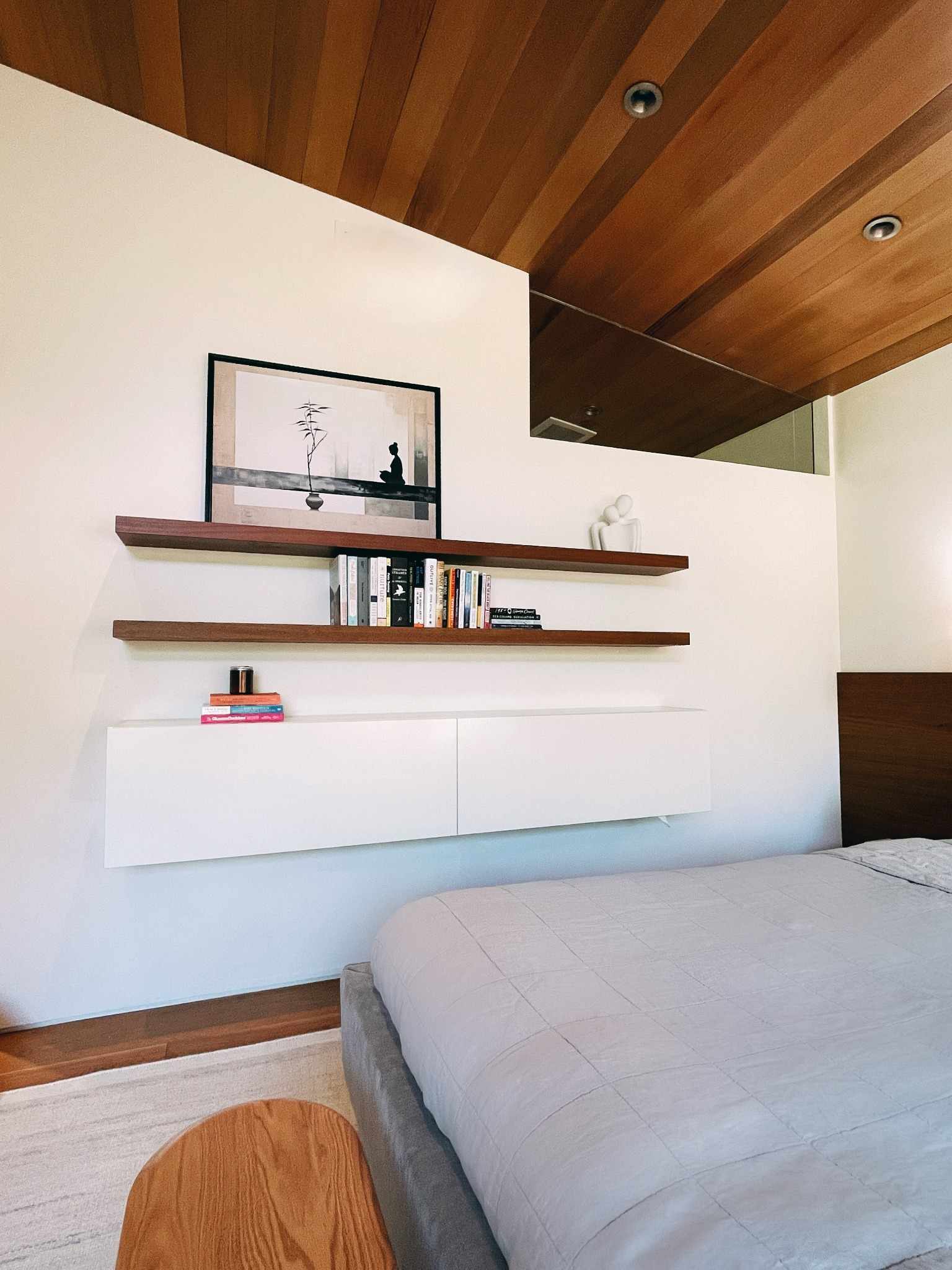 Bedroom wall featuring minimalist floating shelves and carefully curated artwork above bed in Japandi style