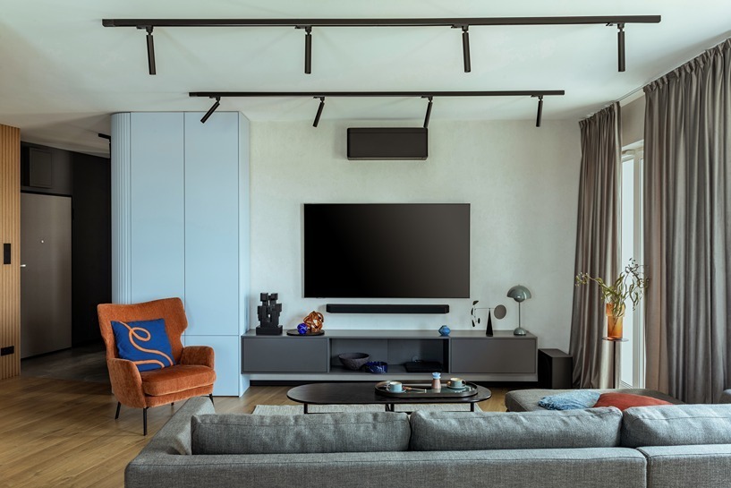 Contemporary media wall under track lighting, featuring a soundbar and an orange accent chair.