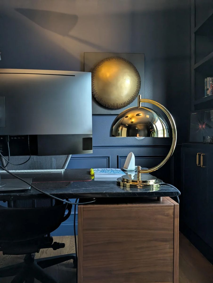 Modern home office with navy blue half-wall wainscoting behind a wooden desk, creating a focused work environment
