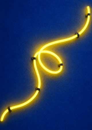 Glowing yellow tube with a central loop and black support clips on a textured cobalt-blue wall.