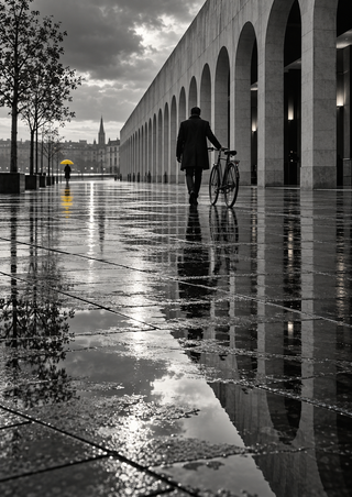 Dark-coated person walking a bicycle across reflective plaza paving, with stone arcades and a distant yellow umbrella.