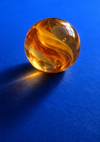 Large translucent amber-orange sphere with swirling internal bands, a small bubble, and bright reflection on a saturated blue ground.