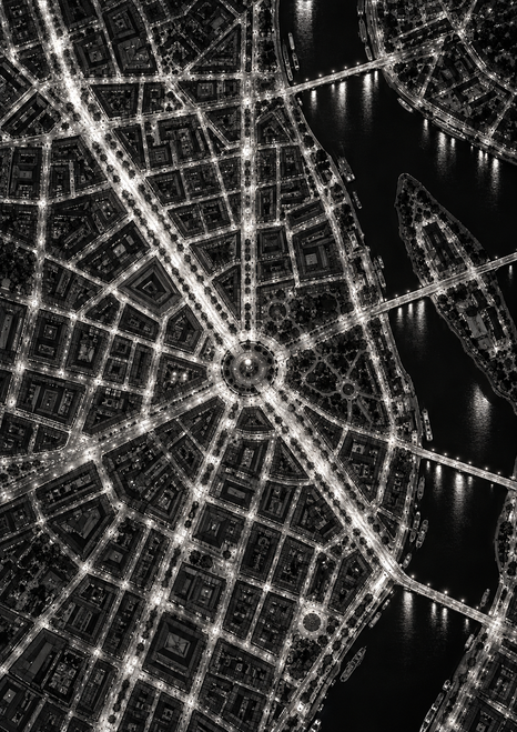 Black-and-white overhead city grid with illuminated diagonal streets converging at a circular plaza beside a dark river crossed by bridges.