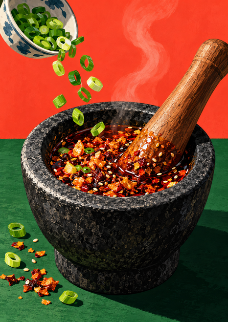 Dark stone mortar of glossy red chili mixture with a diagonal wooden pestle, rising steam, and scallions falling from a bowl.