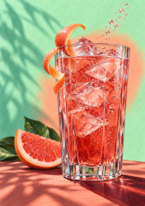 A tall faceted glass of pink-red grapefruit soda with ice, curled peel and bubbles, beside a grapefruit wedge and leaves.